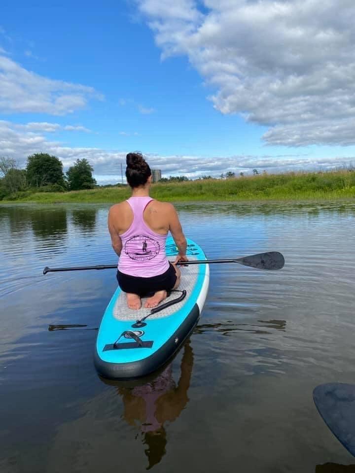 young girl wearing pink tank top sitting on our blue paddleboard. 